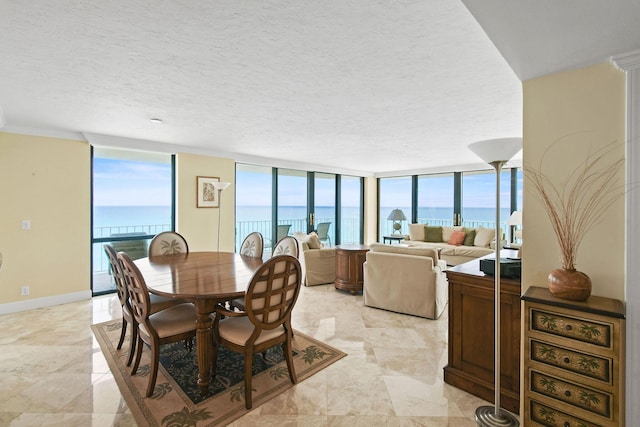 dining room featuring a water view, a wall of windows, baseboards, and a textured ceiling