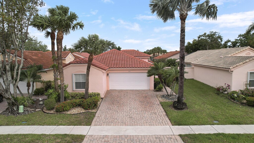 view of front of home featuring stucco siding, an attached garage, a tiled roof, decorative driveway, and a front yard