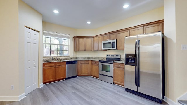 2558 SE Pineland Dr, Port Saint Lucie, FL 34952 - kitchen featuring brown cabinets, light wood-style floors, light stone counters, and stainless steel appliances