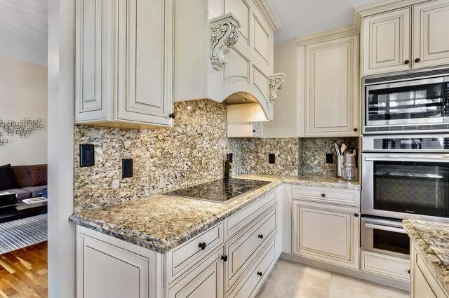 kitchen with cream cabinets, stainless steel appliances, light stone counters, and backsplash