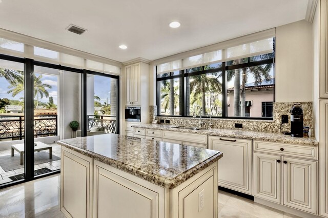 kitchen with a sink, visible vents, light stone countertops, and cream cabinetry