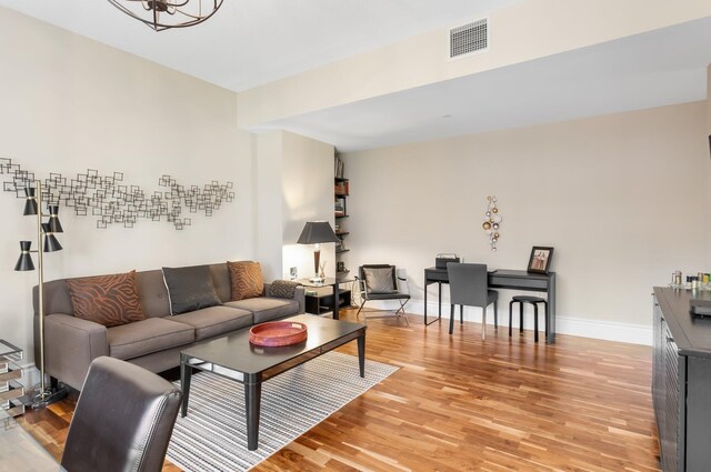 living room featuring visible vents, light wood finished floors, baseboards, and a notable chandelier