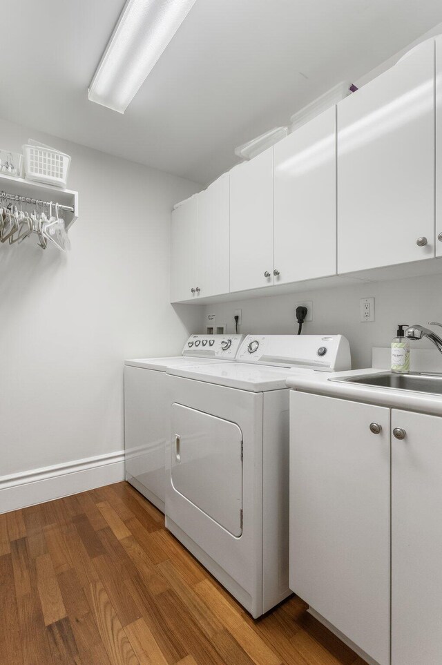 washroom featuring cabinet space, a sink, baseboards, light wood-style floors, and separate washer and dryer