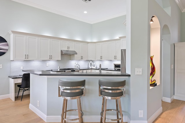 10740 Grande Blvd, West Palm Beach, FL 33412 - kitchen featuring a breakfast bar area, crown molding, under cabinet range hood, dark countertops, and light wood-style floors