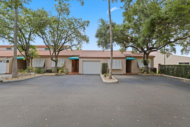 ranch-style house with a garage, stucco siding, a tile roof, and aphalt driveway
