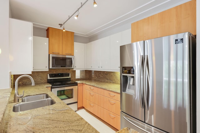 kitchen featuring backsplash, appliances with stainless steel finishes, a sink, light stone counters, and white cabinetry