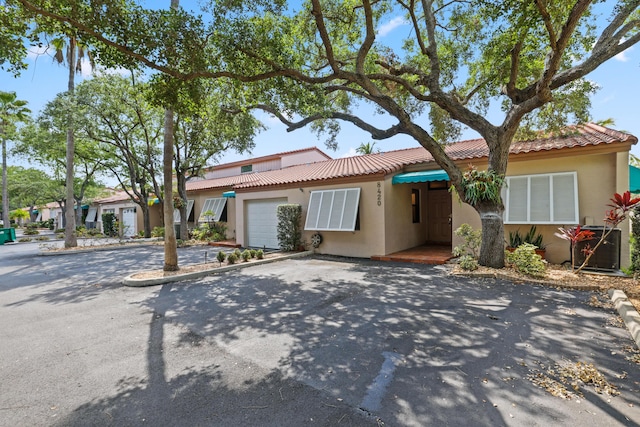 view of front facade featuring central AC, stucco siding, an attached garage, driveway, and a tile roof