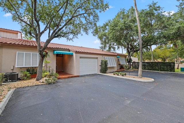 view of front of home with a garage, stucco siding, a tiled roof, central air condition unit, and driveway