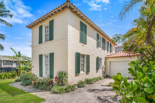 332 Monceaux Rd, West Palm Beach, FL 33405 - view of property exterior featuring stucco siding, a tiled roof, decorative driveway, fence, and a garage