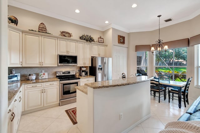 kitchen with a center island, ornamental molding, light tile patterned floors, cream cabinets, and appliances with stainless steel finishes