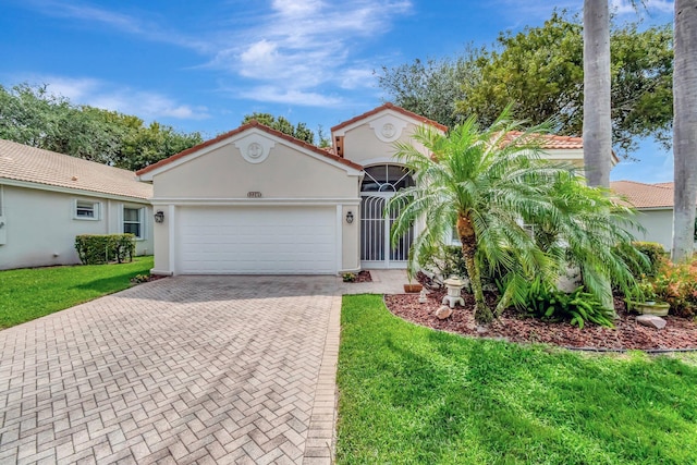 mediterranean / spanish home featuring a tiled roof, an attached garage, a front lawn, and decorative driveway