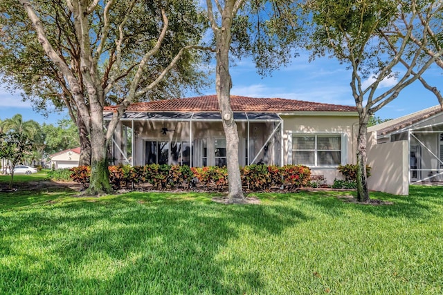 ranch-style home with glass enclosure, a tile roof, a front yard, and stucco siding