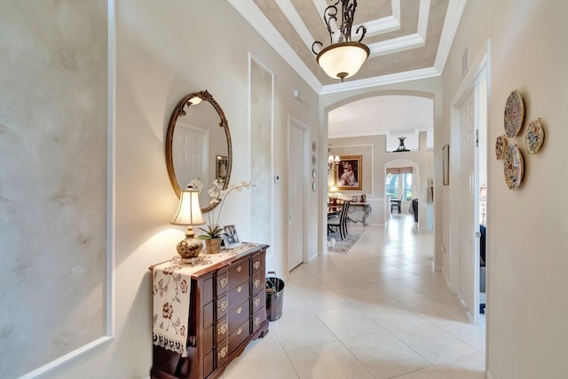 corridor featuring a raised ceiling, arched walkways, ornamental molding, and light tile patterned floors