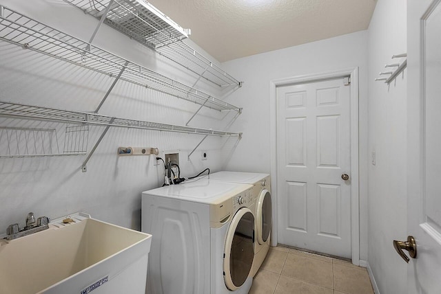 clothes washing area featuring separate washer and dryer, laundry area, a sink, and light tile patterned floors
