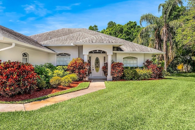mediterranean / spanish house with stucco siding, a shingled roof, and a front lawn