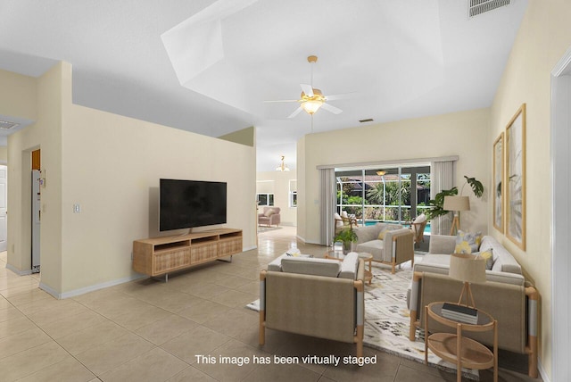 living area with light tile patterned floors, a tray ceiling, visible vents, and a ceiling fan