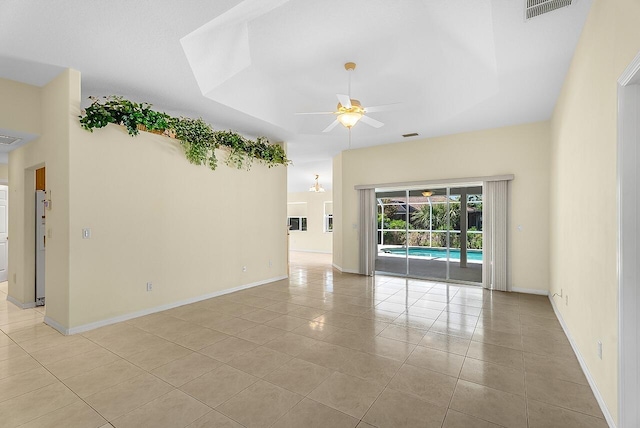 empty room with visible vents, baseboards, a ceiling fan, a tray ceiling, and light tile patterned floors