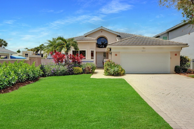 view of front facade featuring stucco siding, an attached garage, a front lawn, a tiled roof, and decorative driveway