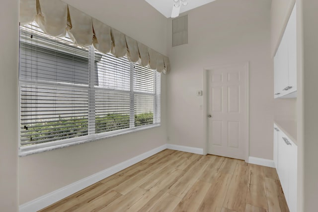 unfurnished dining area featuring light wood finished floors, baseboards, and a high ceiling