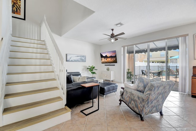 living room featuring a textured ceiling, visible vents, stairs, a ceiling fan, and light tile patterned floors