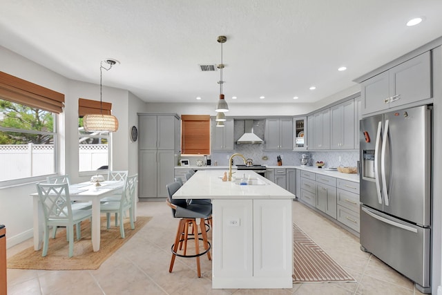 kitchen with light countertops, stainless steel appliances, gray cabinetry, a sink, and wall chimney exhaust hood