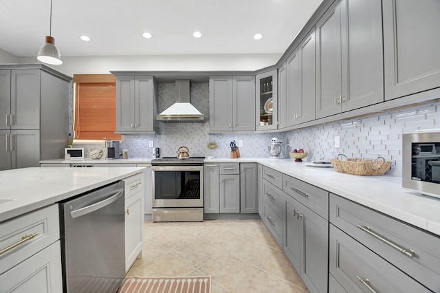 kitchen with gray cabinetry, light countertops, wall chimney range hood, and appliances with stainless steel finishes