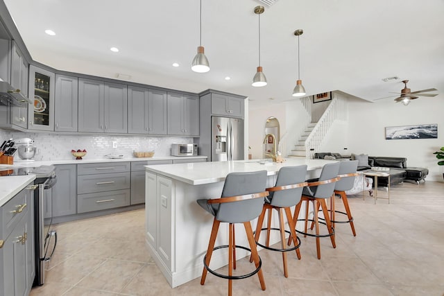 kitchen featuring open floor plan, gray cabinets, decorative backsplash, and appliances with stainless steel finishes