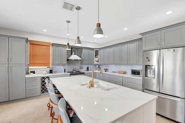 kitchen with gray cabinets, stainless steel appliances, backsplash, a sink, and wall chimney exhaust hood