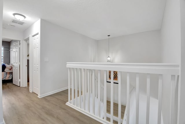 hall with wood finished floors, an upstairs landing, baseboards, and visible vents
