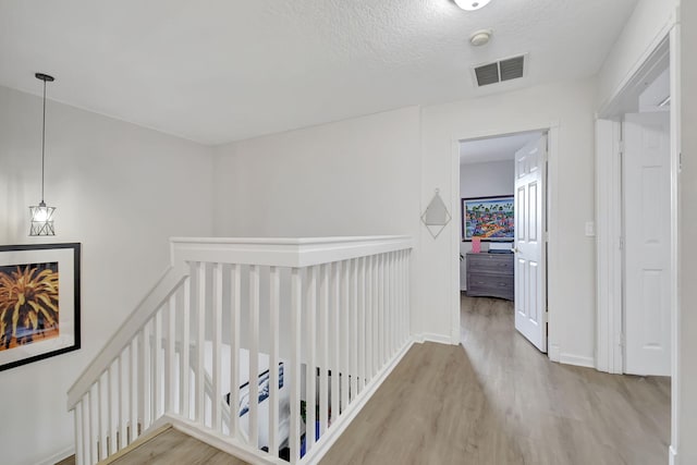 hall featuring a textured ceiling, an upstairs landing, visible vents, baseboards, and wood finished floors