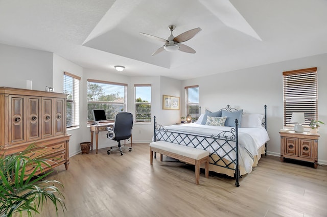 bedroom with baseboards, light wood-style floors, ceiling fan, and a raised ceiling