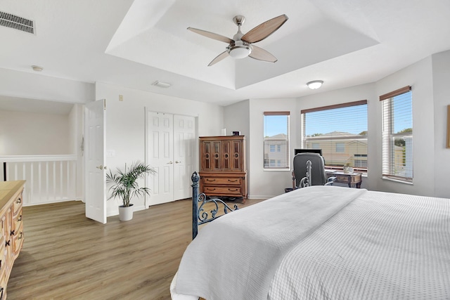 bedroom with light wood-type flooring, baseboards, a raised ceiling, visible vents, and a ceiling fan