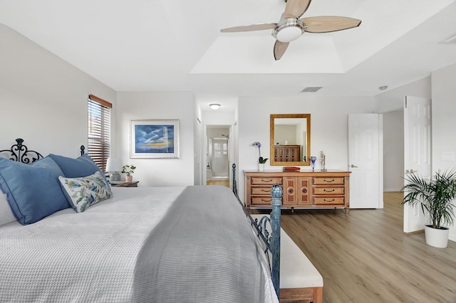 bedroom featuring a tray ceiling, a ceiling fan, wood finished floors, ensuite bath, and visible vents