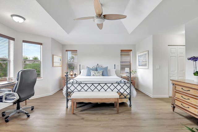 bedroom with baseboards, ceiling fan, a tray ceiling, and light wood-type flooring