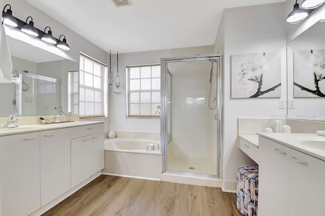 bathroom with a sink, a stall shower, a garden tub, two vanities, and wood finished floors