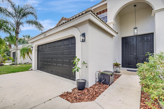 property entrance featuring stucco siding, a tiled roof, a garage, and concrete driveway