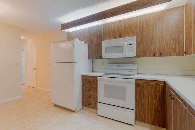 kitchen with brown cabinets, light countertops, baseboards, and white appliances