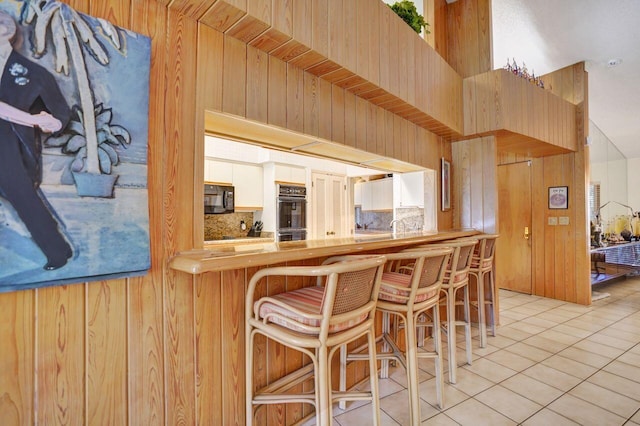 13179 Camero Way, Palm Beach Gardens, FL 33418 - kitchen with black appliances, decorative backsplash, light tile patterned floors, a kitchen breakfast bar, and wooden walls