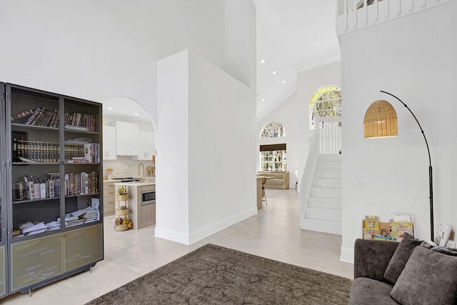 corridor featuring baseboards, high vaulted ceiling, arched walkways, and light tile patterned flooring