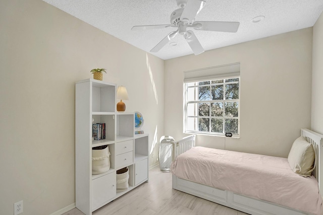 bedroom featuring a textured ceiling, a ceiling fan, light wood-style floors, and baseboards