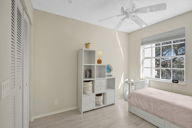 bedroom featuring baseboards, light wood-type flooring, a ceiling fan, and a textured ceiling