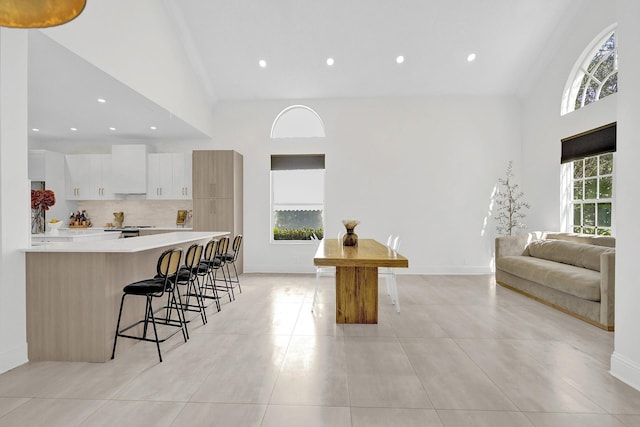 kitchen featuring a kitchen breakfast bar, white cabinets, light countertops, high vaulted ceiling, and backsplash
