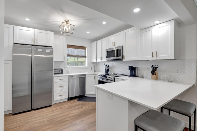 kitchen with white cabinets, a kitchen breakfast bar, a peninsula, light wood finished floors, and stainless steel appliances