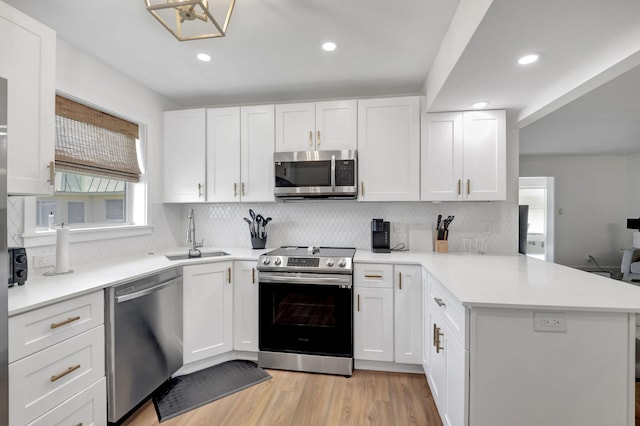 kitchen featuring tasteful backsplash, a sink, light countertops, a peninsula, and stainless steel appliances