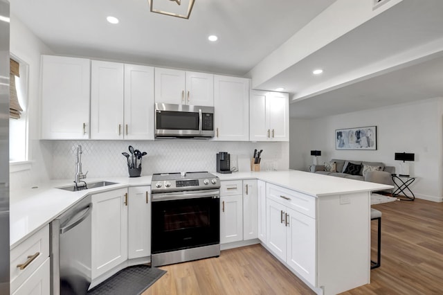 kitchen with a sink, light wood-type flooring, a peninsula, white cabinetry, and stainless steel appliances
