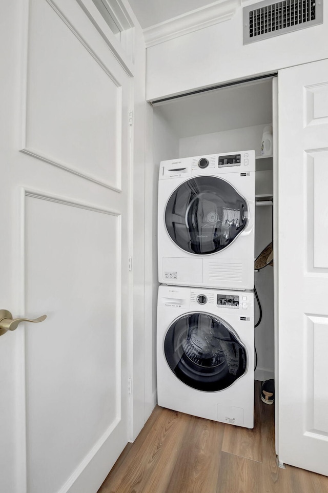laundry area with visible vents, stacked washer and clothes dryer, wood finished floors, and laundry area