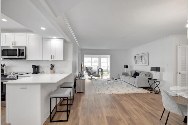 kitchen featuring white cabinets, open floor plan, appliances with stainless steel finishes, light wood-style flooring, and a breakfast bar area