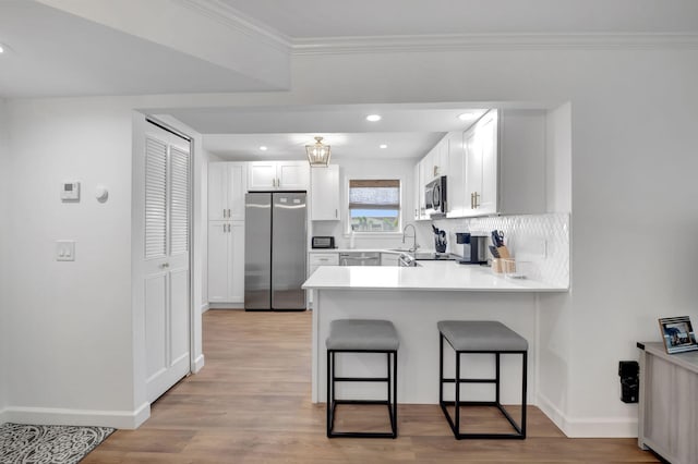 kitchen featuring a peninsula, backsplash, a breakfast bar area, appliances with stainless steel finishes, and light wood finished floors