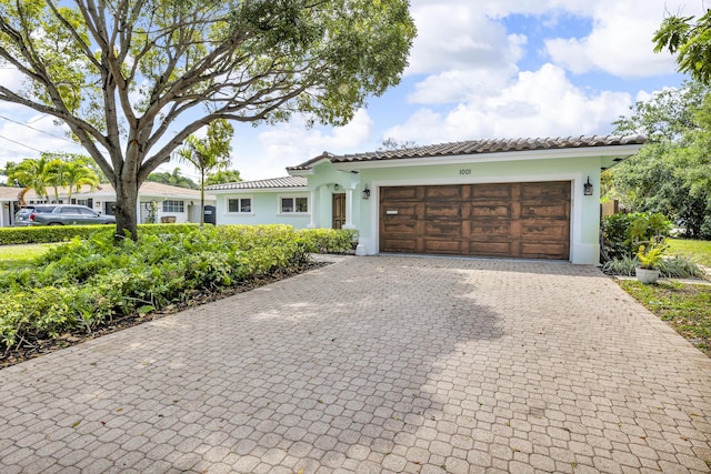 view of front facade with an attached garage, a tiled roof, stucco siding, and decorative driveway