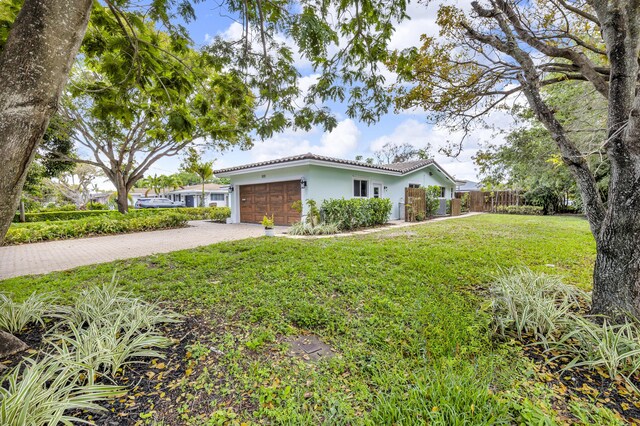 single story home featuring an attached garage, driveway, a tile roof, stucco siding, and a front yard